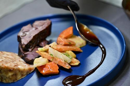 a blue plate with meat and vegetables and a spoon at Das ACKER Hotel in Neuburg an der Donau