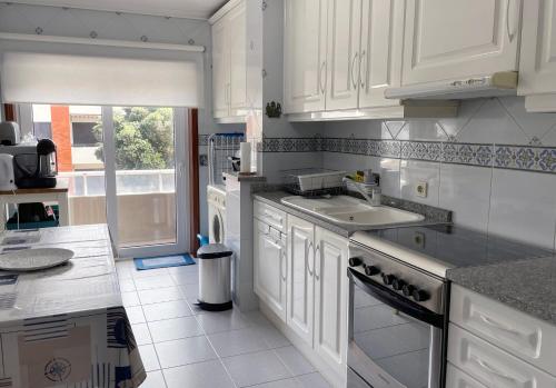 a kitchen with white cabinets and a sink and a window at Barra Azul in Praia da Barra