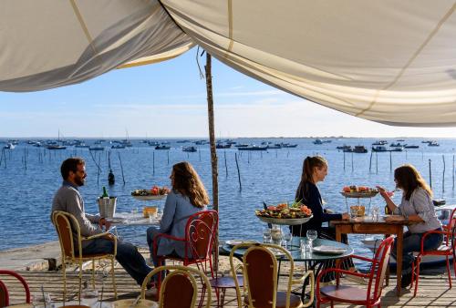 a group of people sitting at a table by the water at Villa Aitama in Cap-Ferret