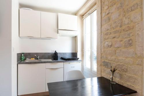 une cuisine avec des placards blancs et un mur en briques dans l'établissement Charmant studio en plein coeur du centre-ville, à Caen