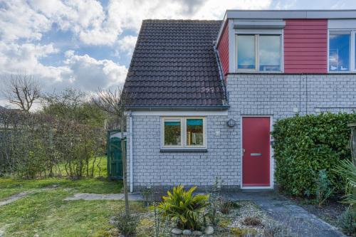 a small white house with a red door at Vakantiehuis, Villapark Oesterbaai 39, aan zee, grenzend aan speeltuin in Wemeldinge