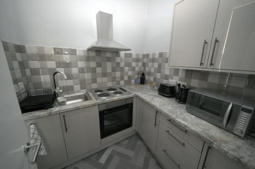 a kitchen with white cabinets and a sink and a microwave at Charming Oxford Apartment in Telford - Flat 1 in Telford
