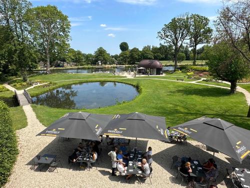 people sitting at tables under umbrellas in front of a pond at Hotel Flora Batava in Breukelen