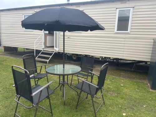 a table with chairs and an umbrella next to a trailer at Seaside Stay in Port Carlisle