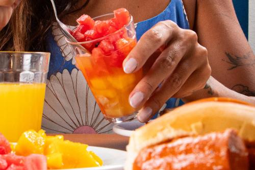 a woman sitting at a table with a glass of fruit at MOVA - Hotel Costa Azul in Ubatuba