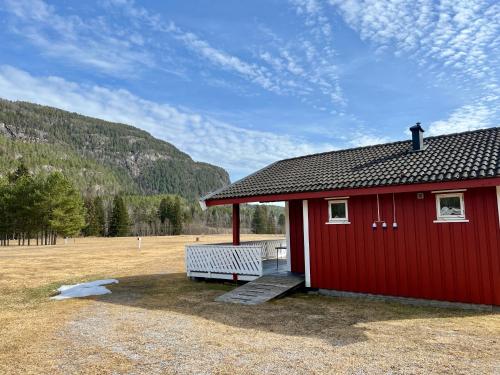 een rood gebouw met een bankje in een veld bij Sanda Camping og Hytteutleie in Øvrebø