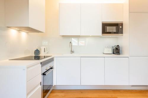 a white kitchen with white cabinets and a microwave at GuestReady - Conde das Alcáçovas in Paço de Arcos