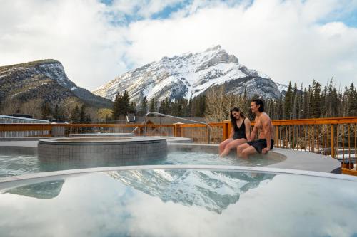 a man and woman sitting in a pool with a mountain at Otter Hotel in Banff
