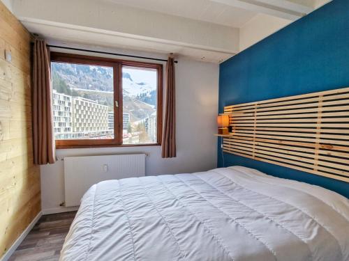 Cet appartement comprend une chambre dotée d'un lit avec un mur bleu et une fenêtre. dans l'établissement Appartement confortable à Flaine - 150m des pistes - 6 pers, balcon, cuisine équipée, lave-linge - FR-1-425-144, à Flaine