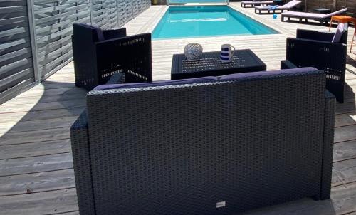 - une piscine avec 2 chaises en osier à côté de la piscine dans l'établissement Maison Petite Bleue piscine privée chauffée, à Lacanau-Océan
