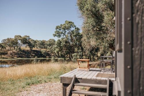 a wooden deck with two chairs sitting on it next to a river at Cosy Off-Grid Cabin with Lake View Pet Friendly - Nikita in Rylstone