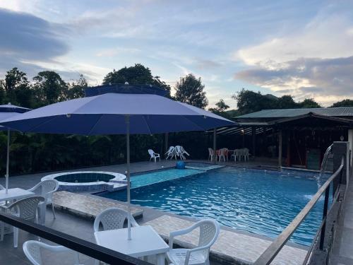 a swimming pool with an umbrella and chairs and a table at Pachaea Hotel campestre in La Vega