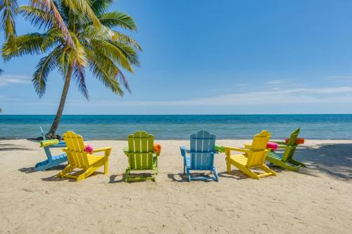 a group of chairs on a beach with a palm tree at Bella Sway Belize in Maya Beach