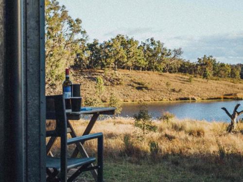 a bottle of wine sitting on a table next to a lake at Lakeside Off-Grid Cabin - Pet Friendly - Freja in Rylstone