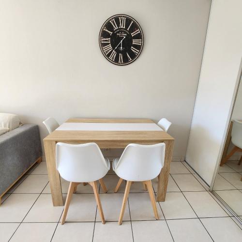 une table avec deux chaises blanches et une horloge sur le mur dans l'établissement Appartement au calme à NICE à proximité de tout !, à Nice