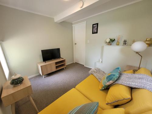 a living room with a yellow couch and a television at Riverside Retreat in Whangarei