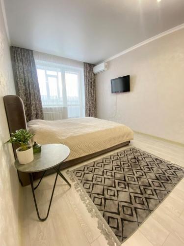 a bedroom with a bed and a table and a tv at Уютные апартаменты в новом жилом комплексе in Kostanay