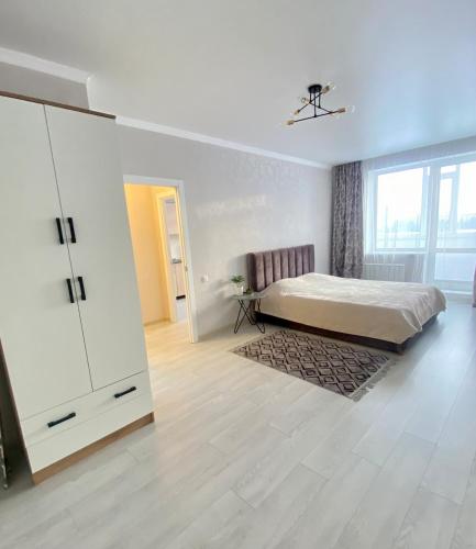 a white bedroom with a bed and a dresser at Уютные апартаменты в новом жилом комплексе in Kostanay