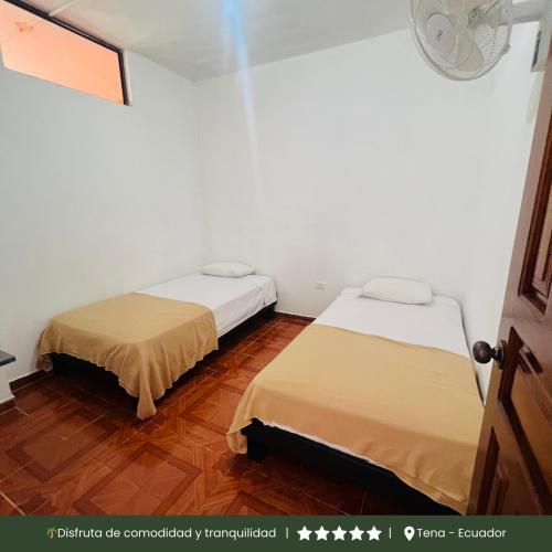 two beds in a room with white walls and wooden floors at RinaKawsay - ViveViajando Apartamento amoblado en Tena in Tena