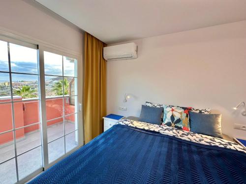 a bedroom with a blue bed and a large window at Sunset Apartment 5 & Heated Pool in Los Cristianos