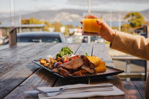 a person holding a glass of orange juice next to a plate of food at Shoreline Hotel in Hobart