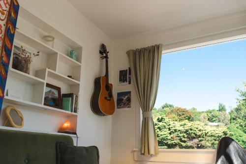 a guitar hanging on a wall next to a window at Sunrays Stay - Stylish Retreat in New Plymouth