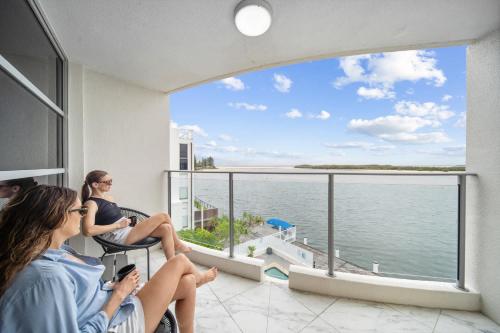 two women sitting on a balcony looking out at the ocean at Pumicestone Passage Waterfront Escape in Caloundra