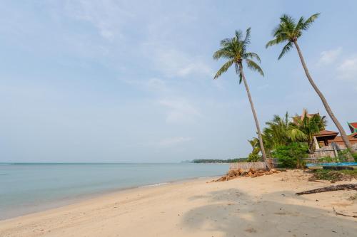 a beach with two palm trees and a house at Sun & Sand Bungalows in Thongsala