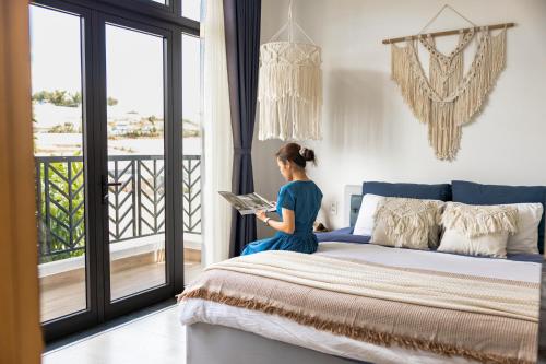 a woman sitting on a bed reading a book at Boho Boutique Da Lat - View nhà lồng lãng mạn in Da Thanh