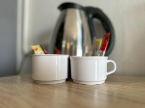 two white cups sitting on a counter with a tea pot at Khaosan Art Hotel in Bangkok