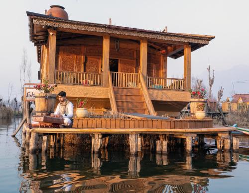a man sitting on a dock with a house on the water at Sukoon Houseboat Dal Lake in Durgjan