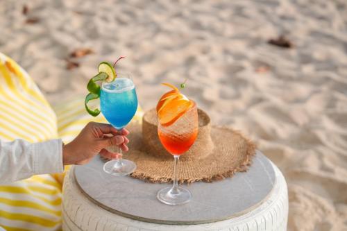 a person holding two cocktails on a table on the beach at BJ & Radisson Sea View Hotel in Ko Yao Yai