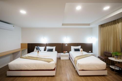 two beds in a hotel room with white walls at Silom Residence Khlonghae Hotel in Hat Yai