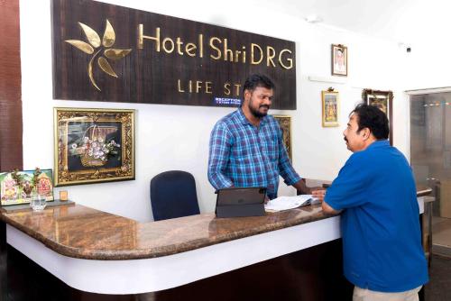 two men standing at a hotel shirmhr dipig counter at Hotel DRG Classic in Tiruppūr