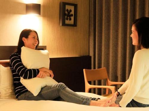 a woman sitting on a bed holding a pillow at Richmond Hotel Yamagata Ekimae in Yamagata