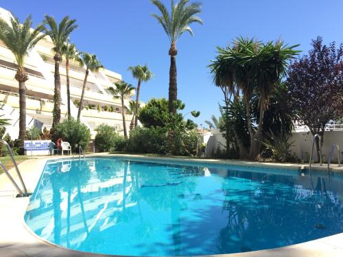 a swimming pool with palm trees and a building at Palmeras del Golf - Torrequebrada in Benalmádena