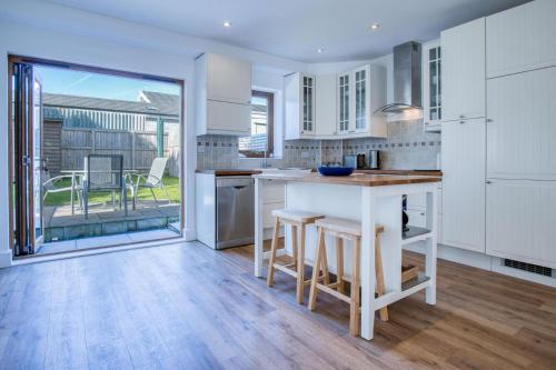 a kitchen with white cabinets and a table with stools at Nottage Road - 3 Bedroom Holiday Home - Mumbles in Swansea