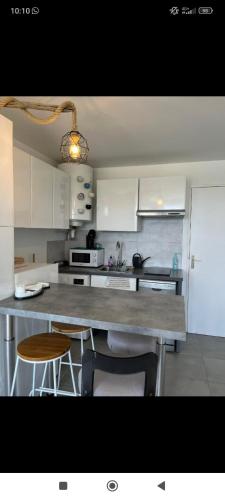 une cuisine avec des armoires blanches et un comptoir avec des tabourets dans l'établissement Studio cabine à Port Camargue, au Grau-du-Roi