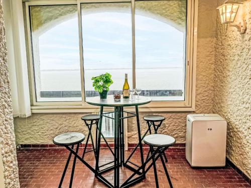 - une table avec une bouteille de vin et des tabourets devant une fenêtre dans l'établissement Studio Coudalère-Guadeloupe-11 by Interhome, au Barcarès