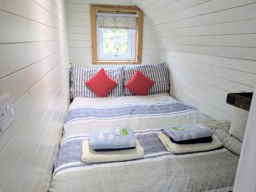 a small bed in a tiny house with red pillows at Pod Beag beside the sea Isle of Eriskay in Eriskay