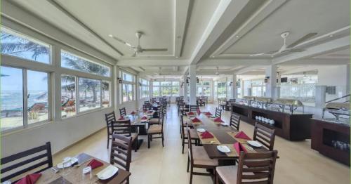 a dining room with tables and chairs and windows at Manara Beach Resort in Bentota