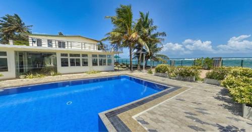 a swimming pool in front of a house with the ocean at Manara Beach Resort in Bentota