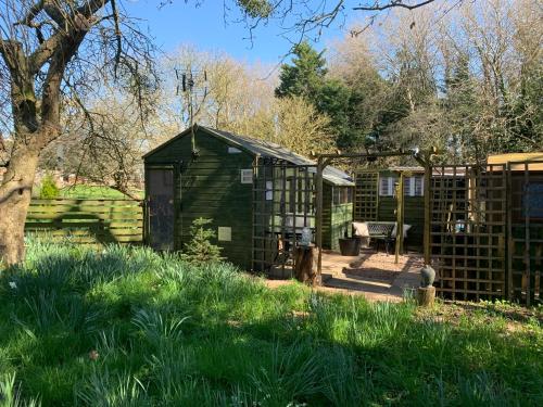 a green greenhouse in a garden with a fence at Hedgehog Lodge in Colwall