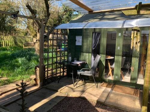 a green shed with a table and a chair at Hedgehog Lodge in Colwall