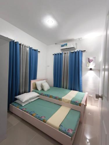 a bedroom with two beds and blue curtains at Rapha's Place Joy - A in Bacolod