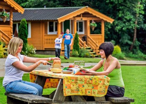 two women sitting at a picnic table in front of a house at Heronstone Lodges in Ystalyfera