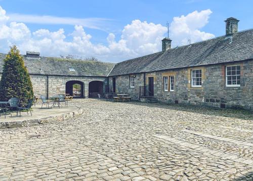 un cortile di un antico edificio in pietra con tavoli e sedie di Mortonhall Park a Edimburgo