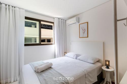 a white bedroom with a bed and a window at Apto Moderno c/ piscina prox. da Praia AVR0203 in Piçarras
