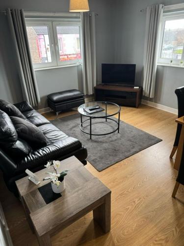 a living room with a leather couch and a coffee table at Kelpies Serviced Apartments- Campbell in Pumpherston