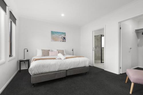 a white bedroom with a bed and a pink chair at Domi Rentals - The Cantala Residence in Clayton North